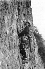 Alpinistka med plezanjem na skali z opremo in varovanjem.