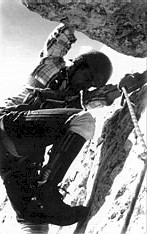 Alpinist med vzponom po skalni steni, varovan z vrvjo.